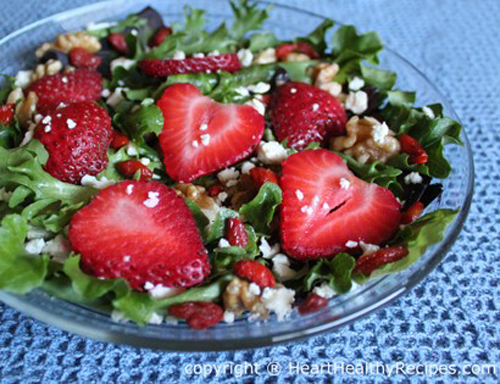 Strawberries and mixed green salad garnished with walnuts and goji berries.
